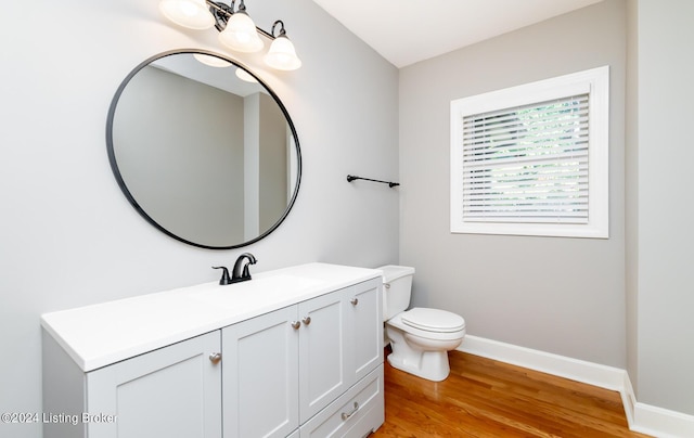 half bath with toilet, baseboards, wood finished floors, and vanity