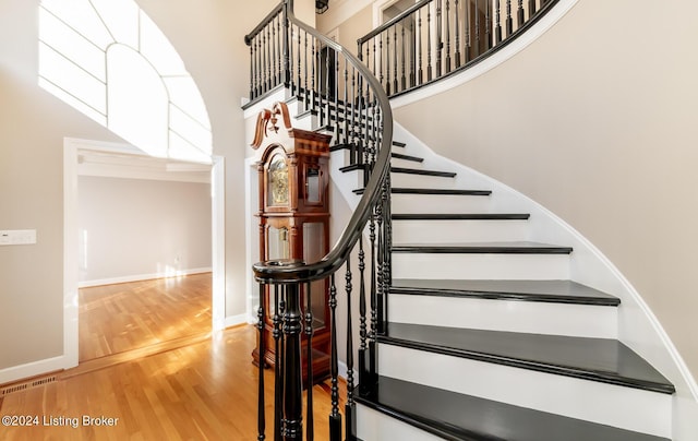 stairway featuring visible vents, wood finished floors, a towering ceiling, and baseboards