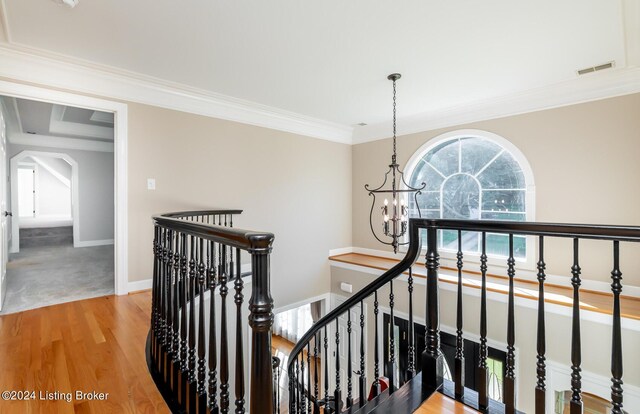 staircase with hardwood / wood-style flooring, ornamental molding, and a chandelier