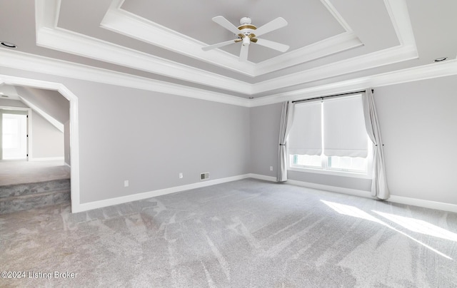 empty room featuring ceiling fan, light carpet, baseboards, a raised ceiling, and crown molding