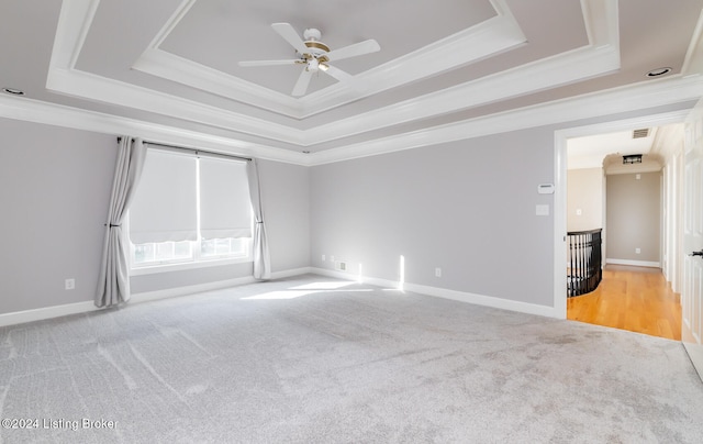 unfurnished room with ornamental molding, ceiling fan, light colored carpet, and a raised ceiling