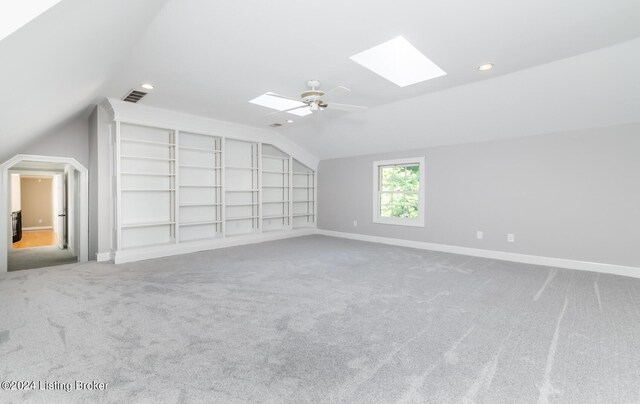 additional living space with lofted ceiling with skylight, built in shelves, carpet flooring, and ceiling fan