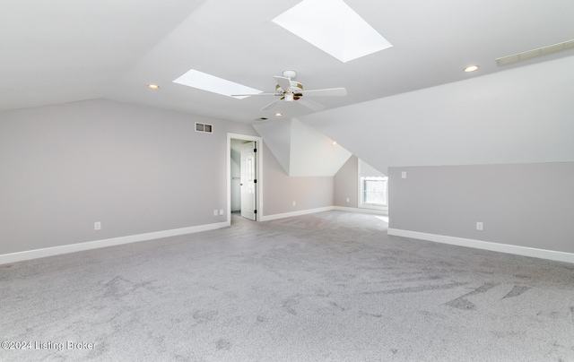 additional living space featuring vaulted ceiling with skylight, visible vents, baseboards, light colored carpet, and ceiling fan