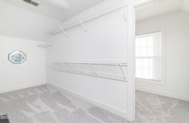 walk in closet featuring lofted ceiling, visible vents, and light carpet