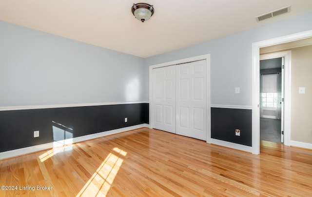 unfurnished bedroom with a closet, wood finished floors, visible vents, and baseboards