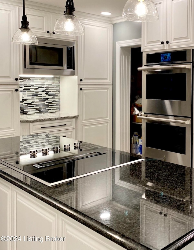 kitchen featuring white cabinetry, stainless steel appliances, decorative light fixtures, dark stone countertops, and decorative backsplash