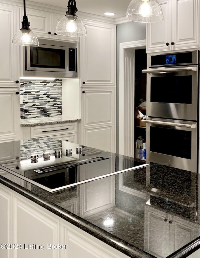 kitchen with stainless steel appliances, white cabinetry, dark stone counters, tasteful backsplash, and decorative light fixtures