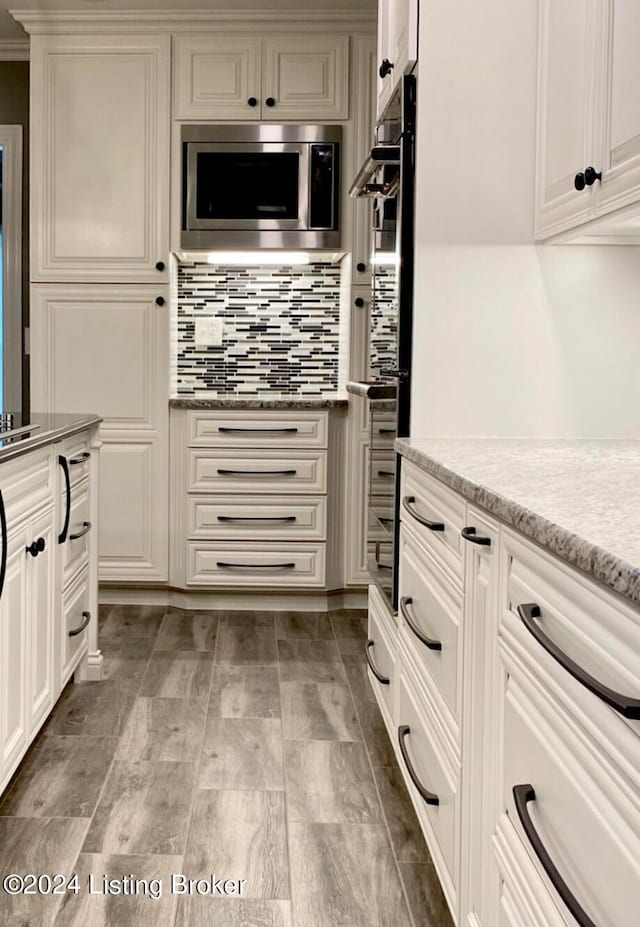 kitchen featuring stainless steel microwave, backsplash, multiple ovens, and white cabinets