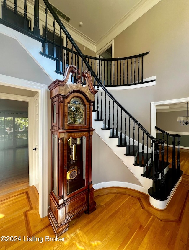 stairway with a towering ceiling, crown molding, wood-type flooring, and a chandelier