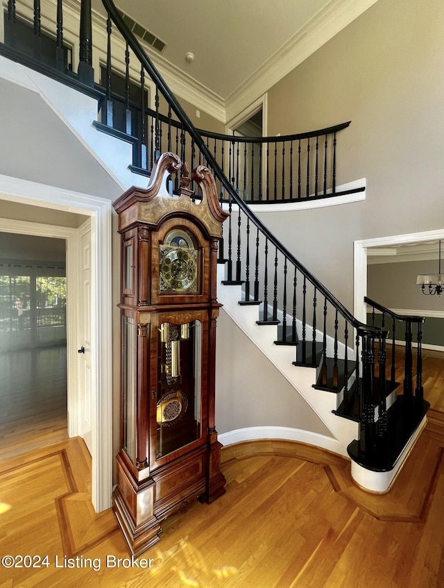 stairs featuring baseboards, visible vents, a towering ceiling, wood finished floors, and crown molding