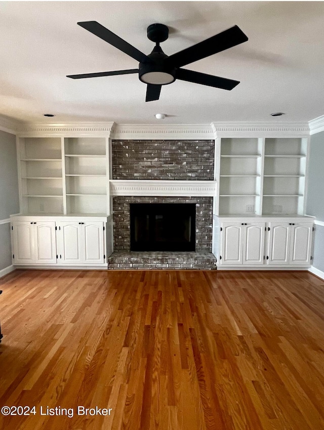 unfurnished living room with ceiling fan, light hardwood / wood-style floors, a brick fireplace, and built in shelves