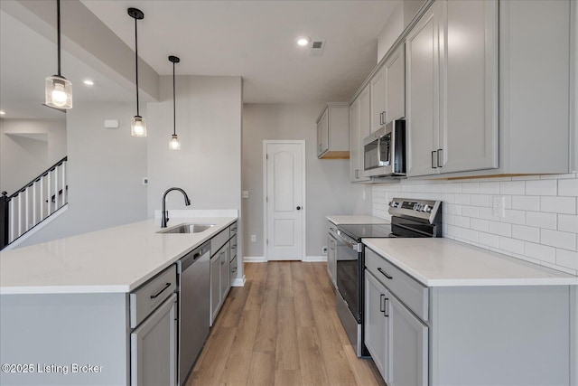 kitchen featuring stainless steel appliances, hanging light fixtures, sink, and gray cabinetry