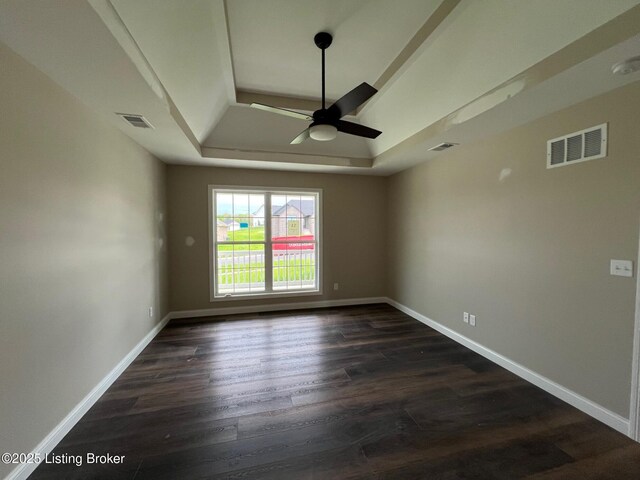 empty room featuring visible vents, ceiling fan, dark wood-style flooring, and a tray ceiling