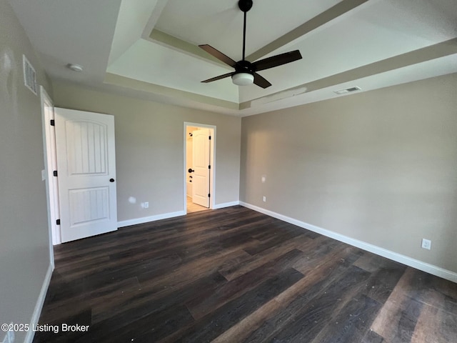 unfurnished bedroom with baseboards, visible vents, dark wood finished floors, and a tray ceiling