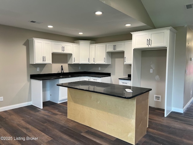 kitchen featuring white cabinetry, a sink, a center island, baseboards, and dark wood-type flooring