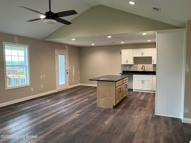 kitchen with dark countertops, a center island, a sink, baseboards, and visible vents
