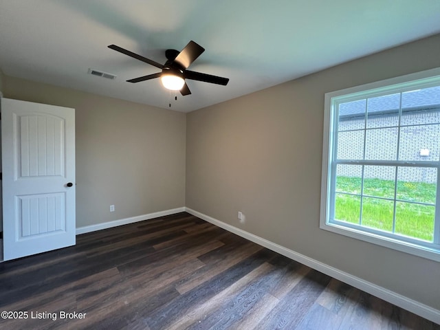 empty room with a wealth of natural light, visible vents, dark wood-style floors, and baseboards