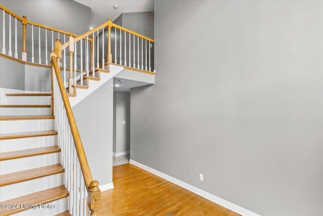 stairs featuring a towering ceiling, baseboards, and wood finished floors