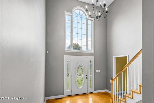 entrance foyer with baseboards, a towering ceiling, an inviting chandelier, stairs, and light wood-style floors