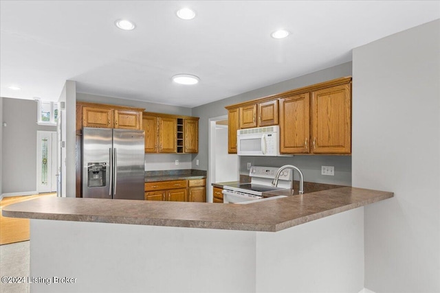 kitchen featuring a peninsula, white appliances, recessed lighting, and brown cabinets