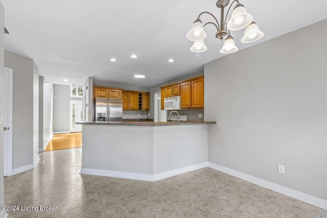 kitchen featuring hanging light fixtures, white microwave, brown cabinetry, high quality fridge, and a peninsula