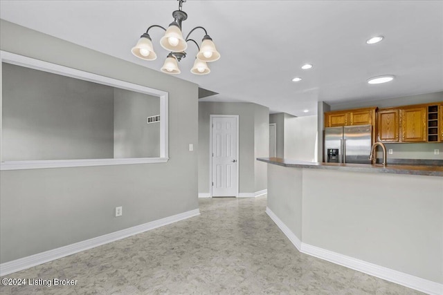 kitchen featuring baseboards, brown cabinetry, high end fridge, decorative light fixtures, and a sink