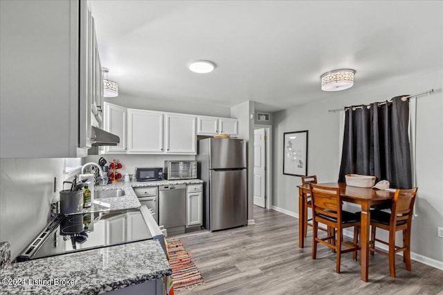 kitchen featuring light stone counters, a sink, white cabinetry, black appliances, and light wood finished floors