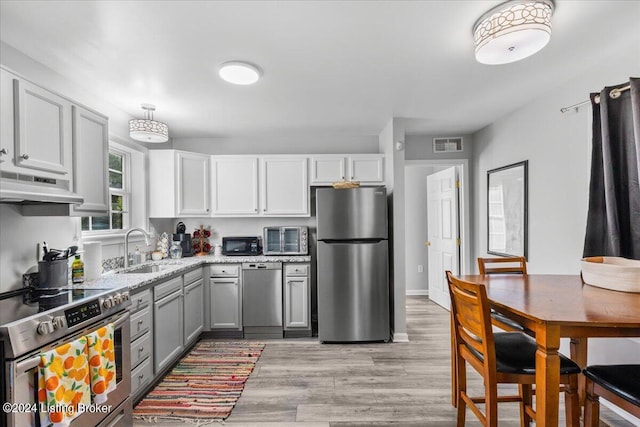 kitchen with visible vents, gray cabinets, stainless steel appliances, under cabinet range hood, and a sink