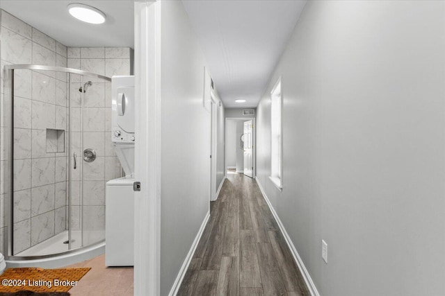 hallway with stacked washer and dryer, wood finished floors, and baseboards