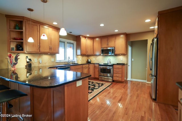 kitchen featuring dark stone counters, a kitchen breakfast bar, decorative light fixtures, kitchen peninsula, and stainless steel appliances