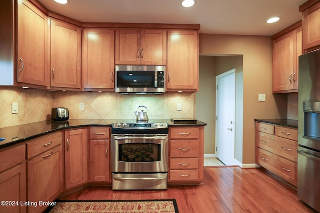 kitchen with light hardwood / wood-style floors, backsplash, appliances with stainless steel finishes, and dark stone counters