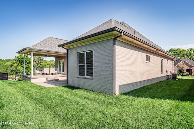 view of property exterior featuring a ceiling fan, central air condition unit, brick siding, a patio, and a yard