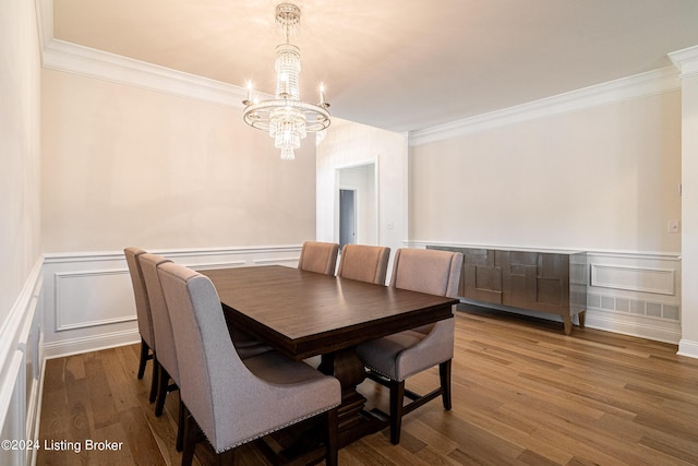 dining area featuring an inviting chandelier, a decorative wall, ornamental molding, and wood finished floors