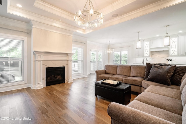 living room featuring a raised ceiling, a fireplace, wood finished floors, ornamental molding, and an inviting chandelier