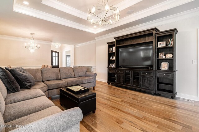 living room with a tray ceiling, a chandelier, crown molding, and light hardwood / wood-style flooring