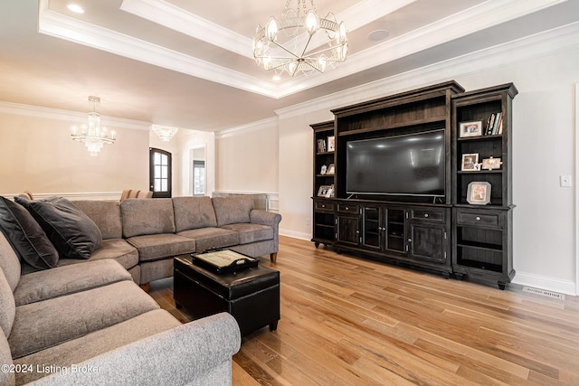 living area featuring a tray ceiling, light wood-style flooring, a chandelier, and crown molding
