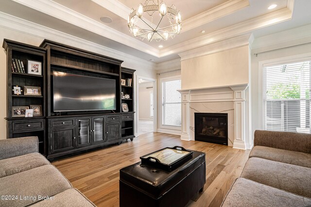 living room with light wood-type flooring, a fireplace, ornamental molding, a chandelier, and a raised ceiling