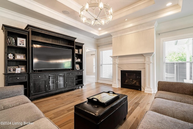 living area featuring a tray ceiling, a notable chandelier, light wood finished floors, and a high end fireplace