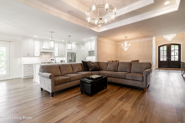 living room with light wood-type flooring, a tray ceiling, crown molding, and a healthy amount of sunlight