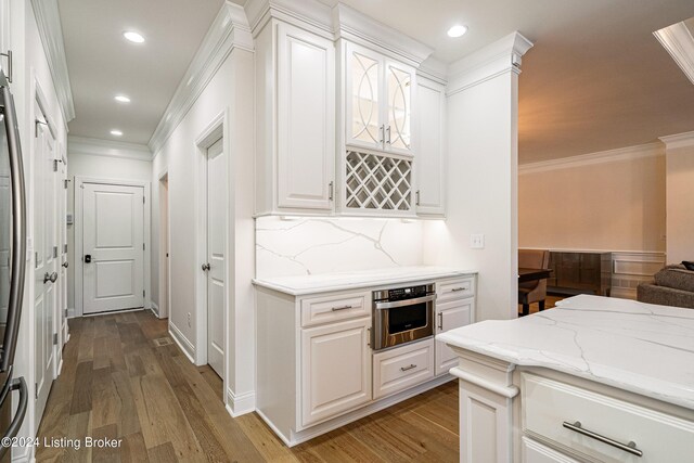 kitchen featuring ornamental molding, wood-type flooring, light stone countertops, stainless steel oven, and white cabinets