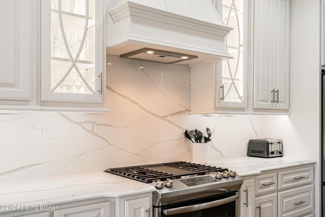 kitchen with premium range hood, stainless steel range with gas cooktop, decorative backsplash, and white cabinetry