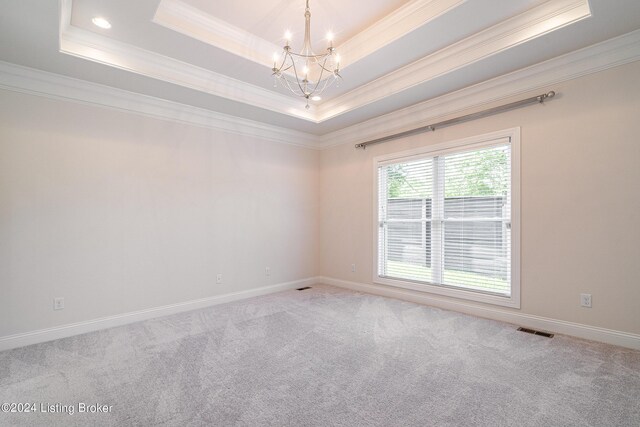 carpeted empty room featuring a tray ceiling, a notable chandelier, and ornamental molding