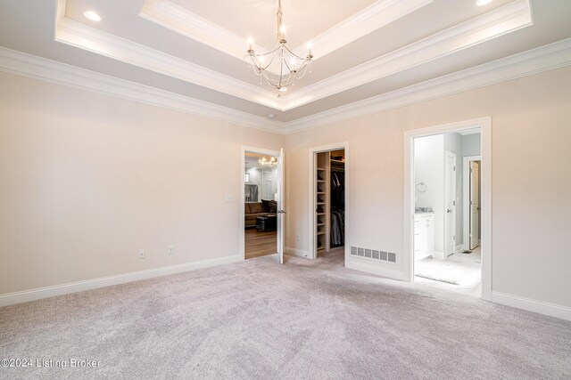 carpeted empty room with crown molding, a raised ceiling, and a chandelier