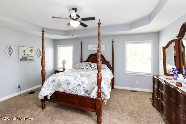 bedroom featuring a tray ceiling, ceiling fan, multiple windows, and light colored carpet