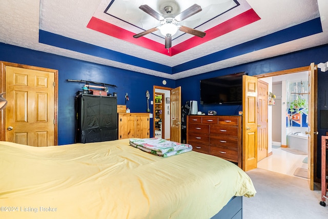 carpeted bedroom with a textured ceiling, a raised ceiling, ceiling fan, and ensuite bathroom