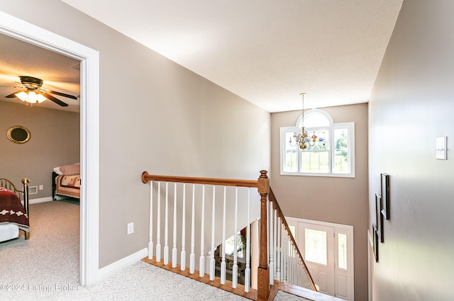 stairway with carpet floors and ceiling fan with notable chandelier