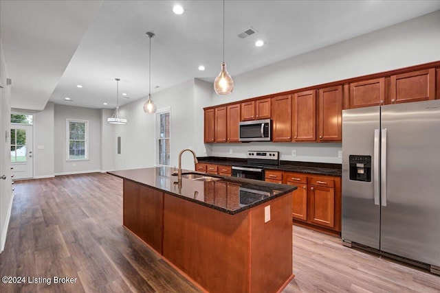 kitchen featuring a kitchen island with sink, dark stone countertops, hardwood / wood-style floors, stainless steel appliances, and sink