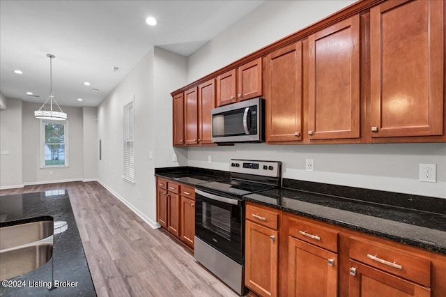 kitchen with light wood-type flooring, appliances with stainless steel finishes, dark stone countertops, and sink