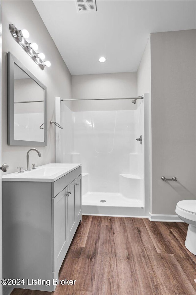 bathroom featuring hardwood / wood-style floors, walk in shower, toilet, and vanity