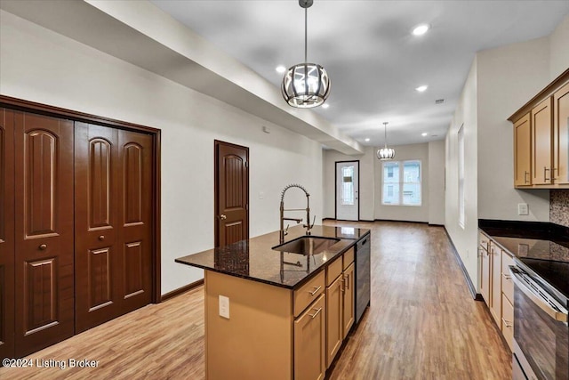 kitchen with light wood-type flooring, dark stone counters, a kitchen island with sink, and sink